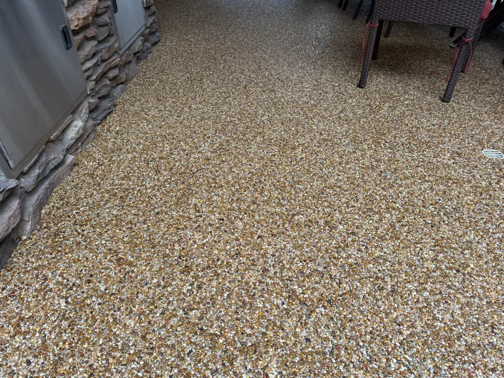 Stone Carpet Patio Flooring – Seamless Pebble Epoxy Overlay Close-up of epoxy stone carpet flooring on an outdoor patio, featuring natural river pebbles bound with UV-stable resin for a seamless, slip-resistant finish.